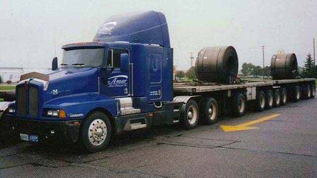 Side view of blue Amar trucking cab hauling chassis with round barrels
