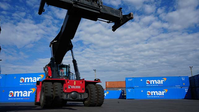 Reach stacker crane parked in front of Amar-owned containers in storage yard