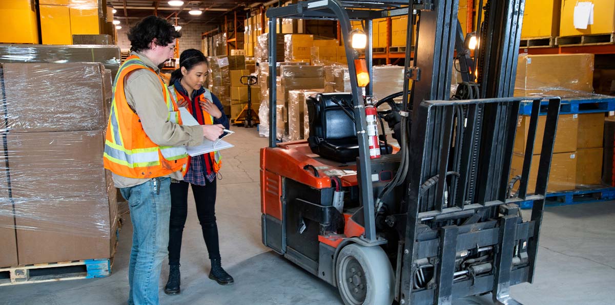 Two Amar warehousing staff reviewing reports beside parked forklift