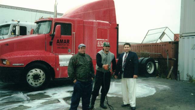 Red 1998 Amar highway cab with three employees standing in front of it