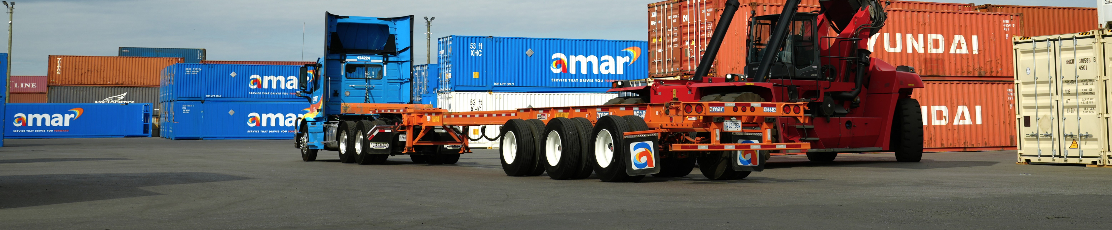 Amar truck with empty chassis parked in container yard beside reach stacker crane