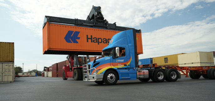 Side view of Amar truck with reach stacker crane loading container onto chassis