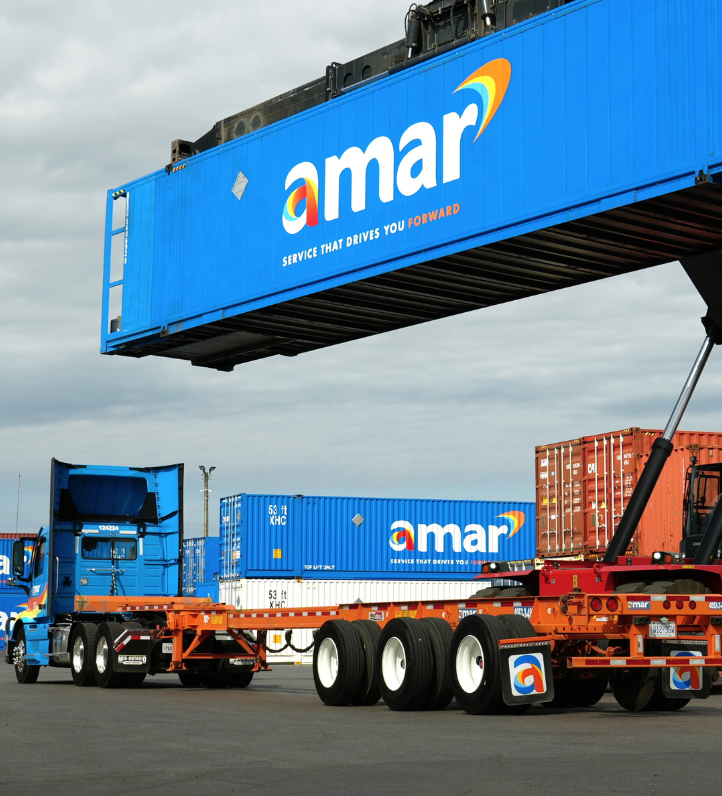 Amar truck with empty chassis parked in container yard beside reach stacker crane